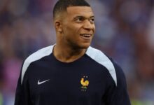 Kylian Mbappé sorrindo, vestindo a camisa azul da França com o logo Nike e emblema FFF.