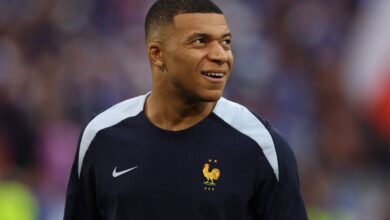 Kylian Mbappé sorrindo, vestindo a camisa azul da França com o logo Nike e emblema FFF.