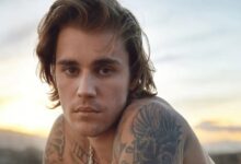 Cantor Justin Bieber sem camisa, com cabelos ondulados e tatuagens no ombro e pescoço.